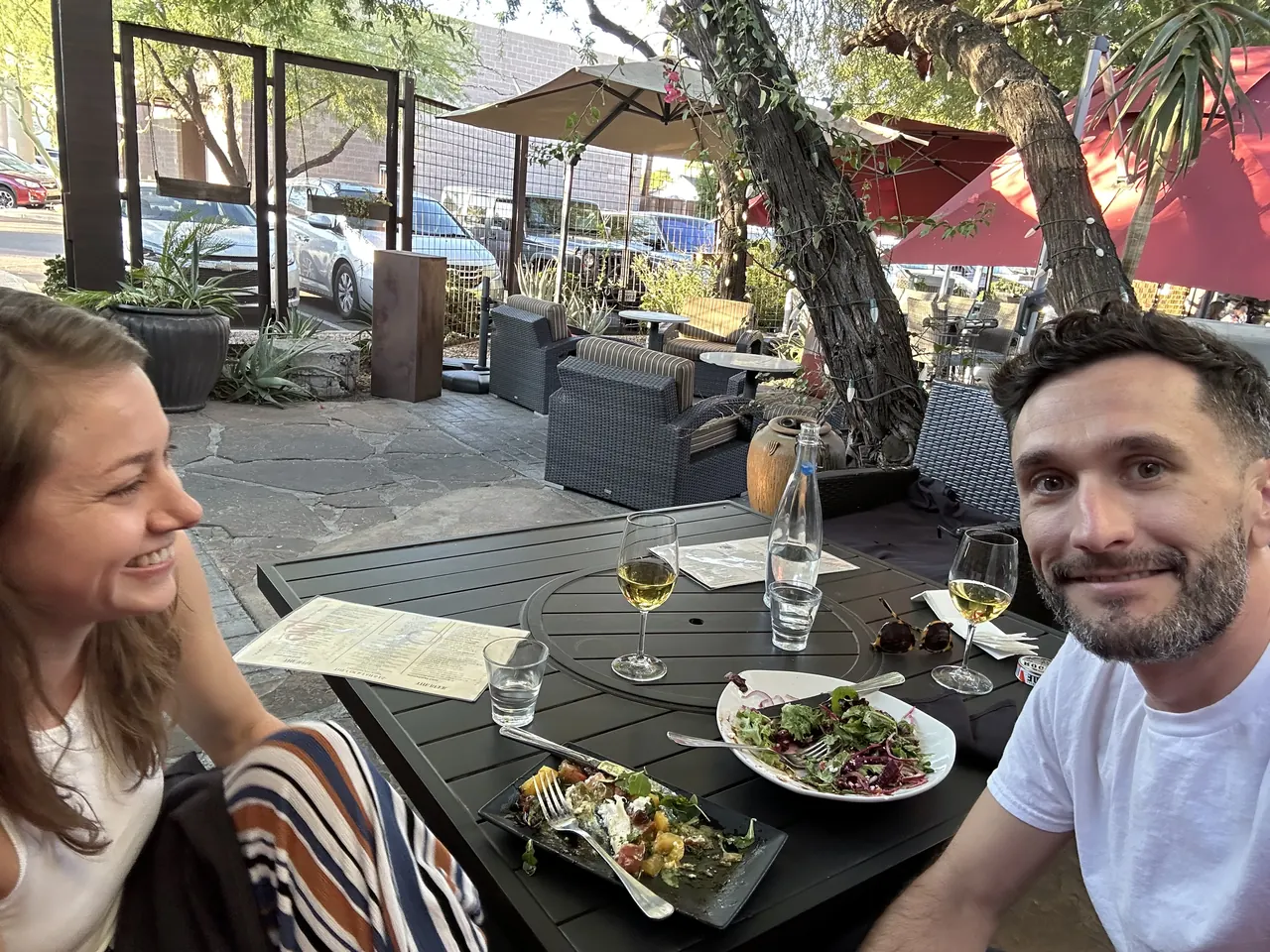 Robbie and a friend smiling over wine and salads on a restaurant patio