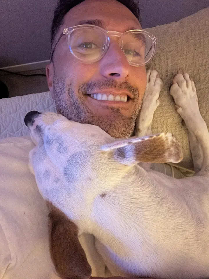 Robbie in glasses smiling, with a white dog curled up beside him