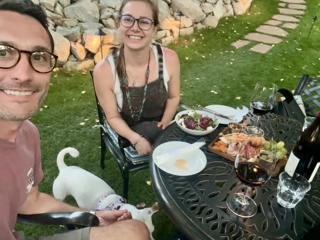 Robbie and a friend with wine and a cheese board on the lawn, a white dog nearby