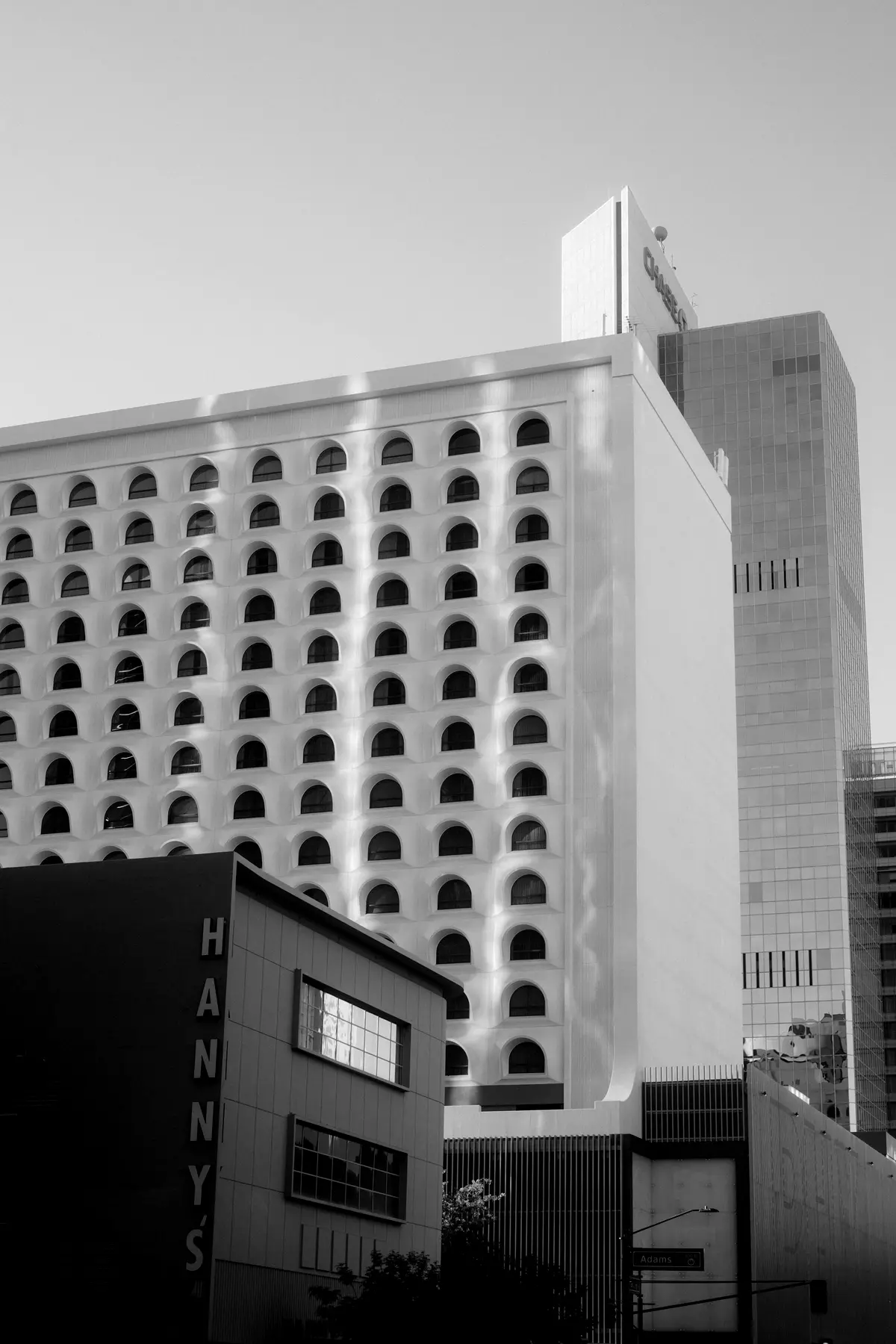 A white Phoenix high-rise covered in rows of arched windows, with the Hanny's sign in the foreground, in black and white